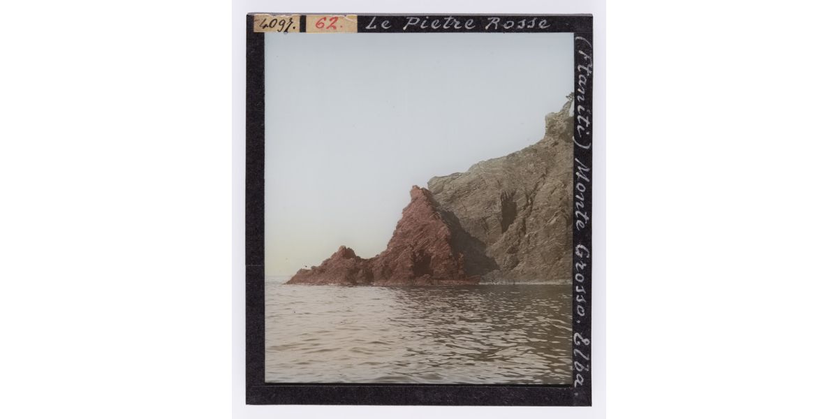 Giorgio Roster, “Le pietre rosse (ftaniti), Monte Grosso. Elba.”, 1902, diapositiva su lastra di vetro colorata a mano, 9 x 8 cm, Archivi Alinari-archivio Roster, Firenze